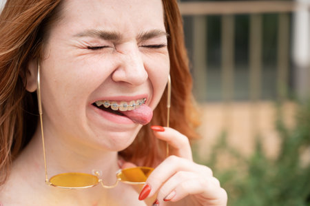 Young woman with braces on her teeth smiles and shows her tongue outdoorsの写真素材