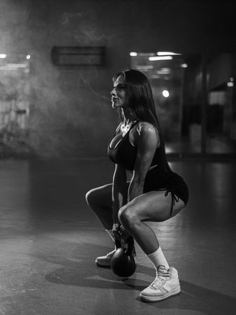 Caucasian woman squats with a kettlebell in the gym. Vertical photoの写真素材