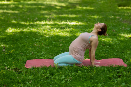 Pregnant caucasian woman doing yoga in the park. Back bendの写真素材