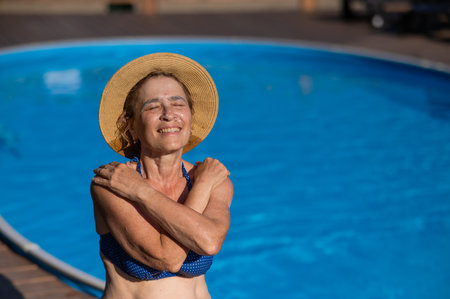 An elderly woman in a straw hat is sunbathing by the pool. Retiree on vacationの写真素材