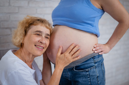 An elderly woman leans against the belly of her pregnant daughter. Close-upの写真素材