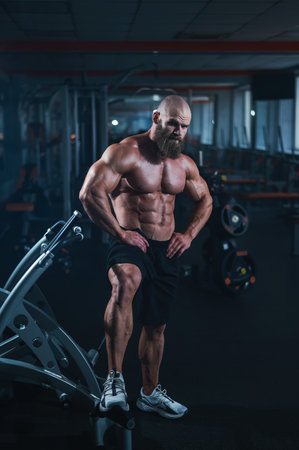Muscular bald man posing in shorts. Bodybuilder showing off his shape in the gymの写真素材