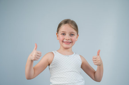 Caucasian 6 year old girl showing thumbs up against white backgroundの写真素材