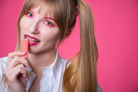 Portrait of a young woman with braces and bright makeup chewing gum on a pink backgroundの写真素材