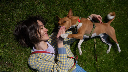 Top view of beautiful young woman and african basenji dog lying on green grassの写真素材