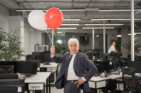Portrait of a cheerful mature business man holding balloons in the officeの写真素材