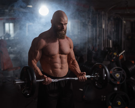 Caucasian bald topless man doing an exercise with a barbell in the gym. Bicep curls with weightsの写真素材
