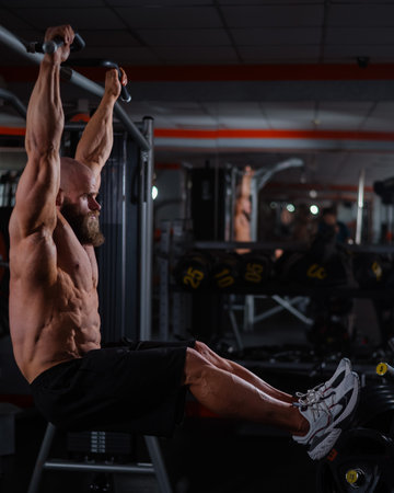 A Caucasian man hangs on a horizontal bar and raises his legs. Vertical photoの写真素材