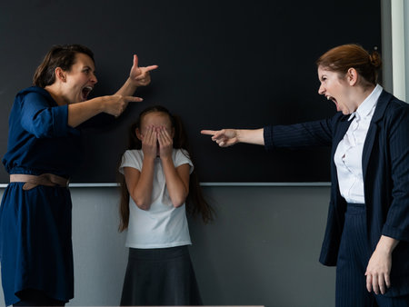 The female teacher screams at the schoolgirl and her mother standing at the blackboardの写真素材