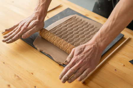 Close-up of a potters hands rolling out clay using a rolling pin with patterns