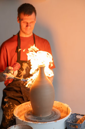 A potter burns a jug with a gas burner on a potters wheel. Vertical photo