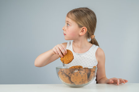 A little girl eats cookies from the tableの写真素材