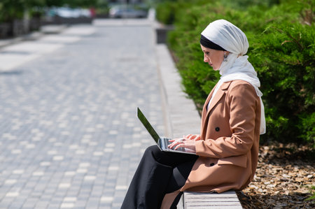 Portrait of young woman in hijab using laptop outdoorsの写真素材