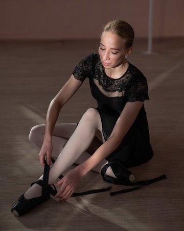 Woman sitting on the floor and tying ribbons on her pointe shoes. Vertical photo