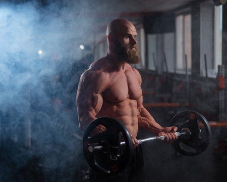 Caucasian bald topless man doing an exercise with a barbell in the gym. Bicep curls with weightsの写真素材