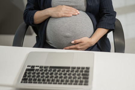A pregnant woman works on a laptop in the office. Close-up of the tummy
