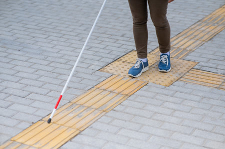Close-up of a woman's legs with a cane near a tactile tileの写真素材