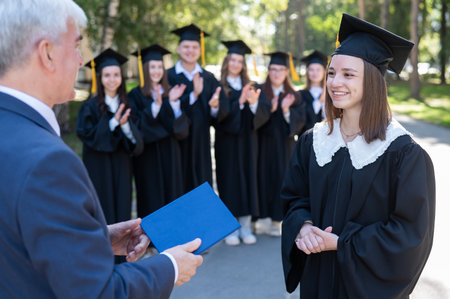 The teacher shakes hands with the student and presents the diploma outdoors. A group of university graduatesの写真素材