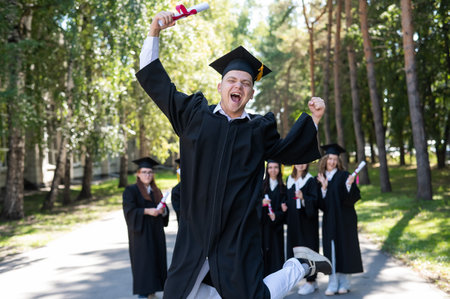 Happy young caucasian man celebrating graduation. Crowd of students graduates outdoorsの写真素材