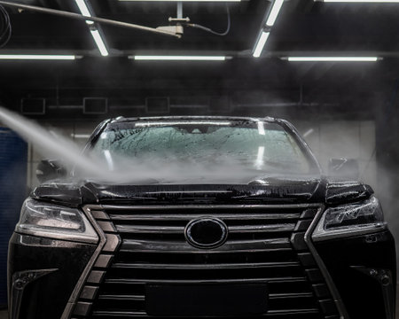 A man washes foam off a black car with water at a car washの写真素材