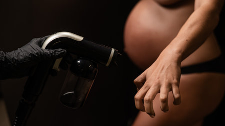 The master applies bronzer with a spray on the hands of a pregnant woman. Instant tanの写真素材