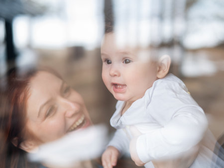 View through the window of a red-haired Caucasian woman holding her little sonの写真素材