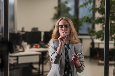 Caucasian woman writing pyramid diagram with questions on glass wallの写真素材