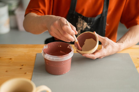 Close-up of a potters hands with a brush painting ceramic dishes