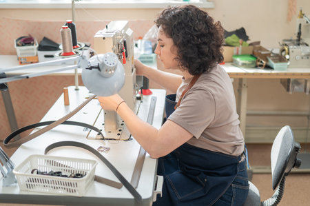 A woman tanner sews a leather belt on a sewing machineの写真素材