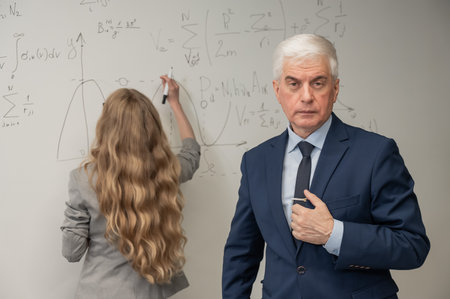 Female student answers a question from an elderly professor at a white boardの写真素材