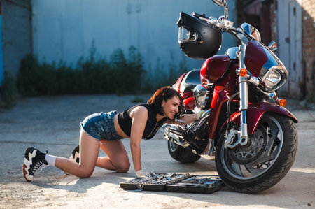 Brunette woman in denim shorts repairs a red motorcycleの写真素材