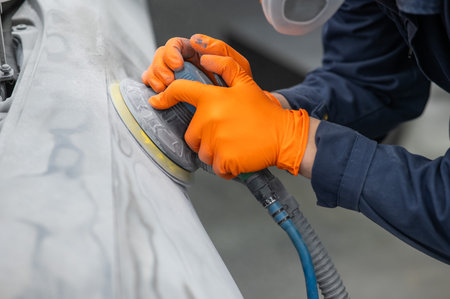 A mechanic sands the putty on a car body with a machine. Repair after an accident