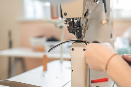 A woman tanner sews a leather belt on a sewing machine. Close-up of hands