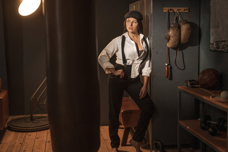 Caucasian woman in a Peaky Blinders style mens suit posing in a retro gymの写真素材