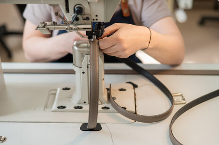 A woman tanner sews a leather belt on a sewing machine. Close-up of hands