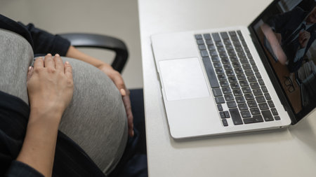 A pregnant woman works on a laptop in the office. Close-up of the tummyの写真素材
