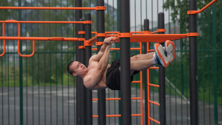 Shirtless male athlete doing front hang on horizontal bar outdoors