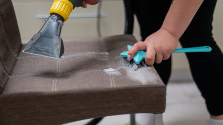 Woman cleaning a fabric chair using a professional washing vacuum cleaner and brush