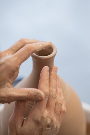 Close-up of a potters hands making a ceramic vase on a potters wheel. Vertical photo