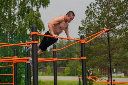 A shirtless man is doing a workout on the horizontal bars outdoors