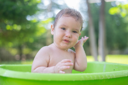 Unhappy boy bathes in a basin outdoors in summerの写真素材