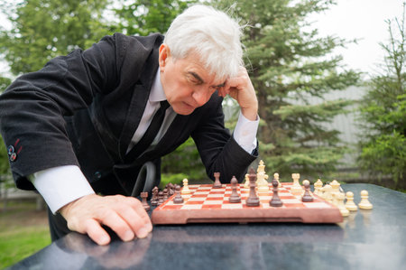 Unhappy elderly man looking at chessboard outdoors