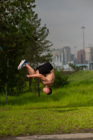 Young shirtless male athlete doing backflip on outdoors. Vertical photo