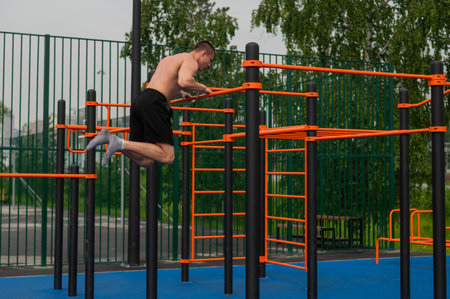 A shirtless man is doing a workout on the horizontal bars outdoors