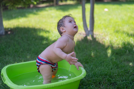 Unhappy boy bathes in a basin outdoors in summerの写真素材