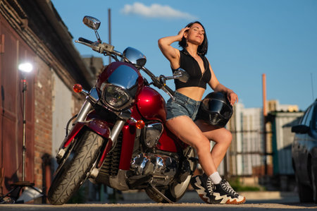 Brunette woman in shorts posing on a red motorcycle
