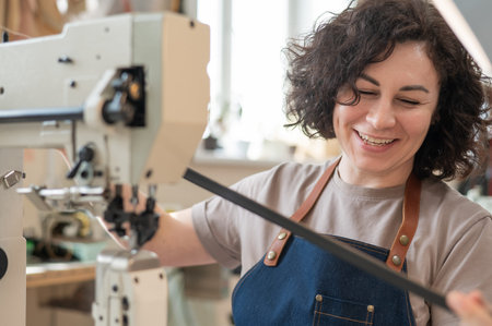 A woman tanner sews a leather belt on a sewing machineの写真素材