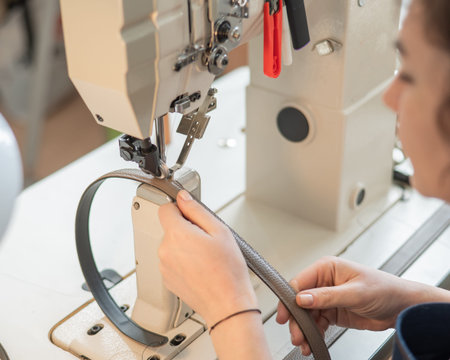 A woman tanner sews a leather belt on a sewing machine