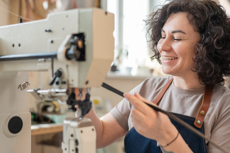 A woman tanner sews a leather belt on a sewing machineの写真素材