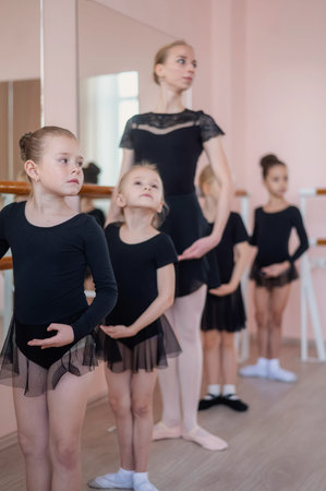 Caucasian woman teaches little girls ballet at the barre. Vertical photo